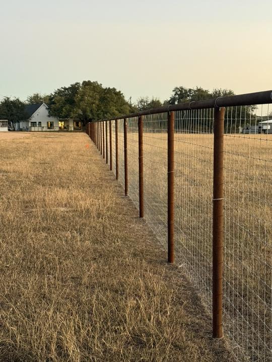 Pipe top rail fence with woven wire at dusk