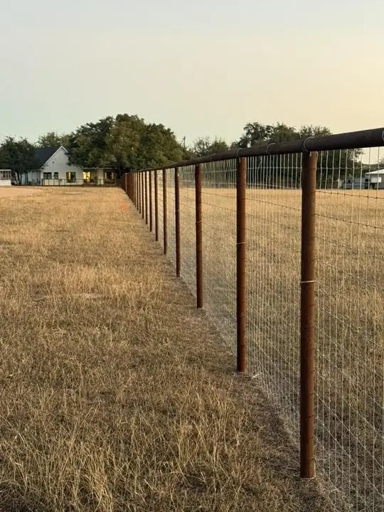 Pipe top rail fence with woven wire at dusk
