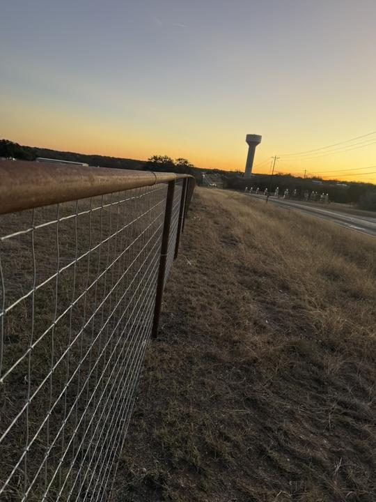 Pipe top rail and wire fence at sunset