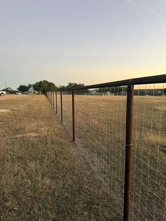 Pipe post and wire ranch fence at sunset